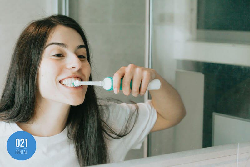 Mulher escovando os dentes em frente ao espelho