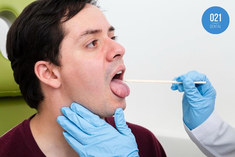 Homem tendo sua língua examinada por dentista 