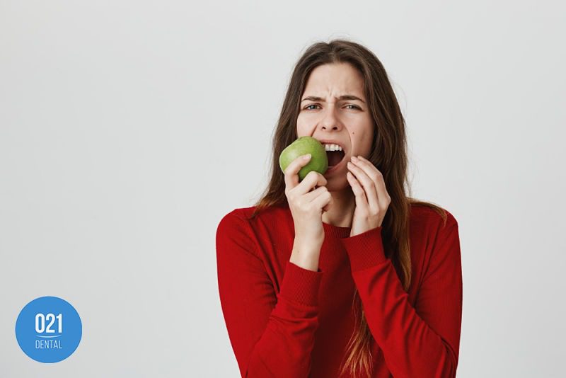mulher mordendo maçã e sentindo dor no dente