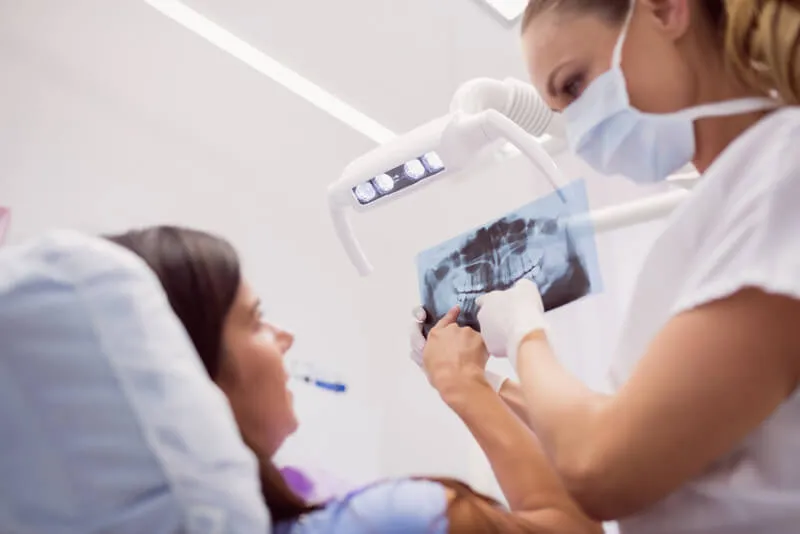 Imagem com paciente e médica conversando na cadeira do dentista sobre uma panorâmica da boca