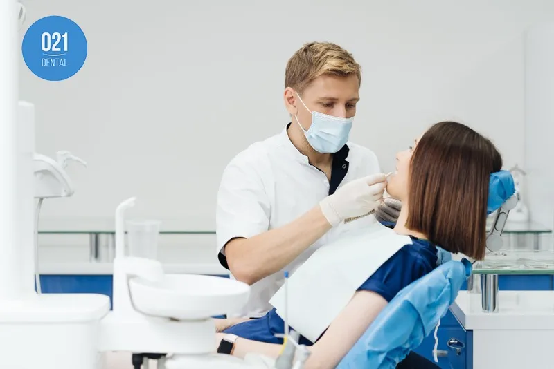 Imagem de um dentista cuidando da saúde bucal de sua paciente em seu consultório esterilizado