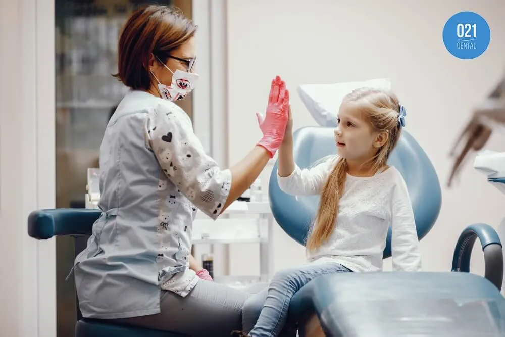 Imagem de uma dentista dando um cumprimento "hi-5" para sua paciente infantil