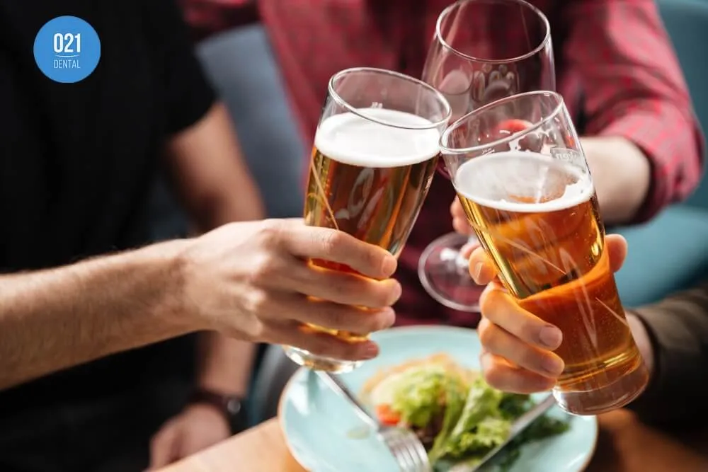 Duas mãos segurando copos de cerveja e uma mão segurando uma taça de vinho enquanto brindam