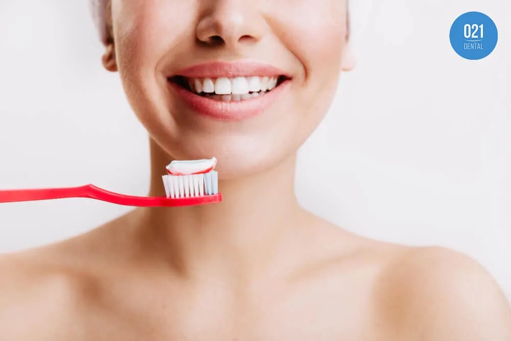 Metade inferior do rosto de uma mulher que está sorrindo e segura uma escova de dentes vermelha