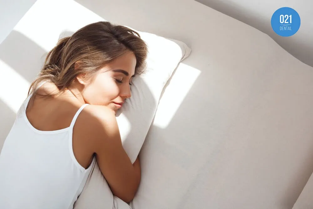 Mulher jovem com regata branca dormindo abraçada em um travesseiro