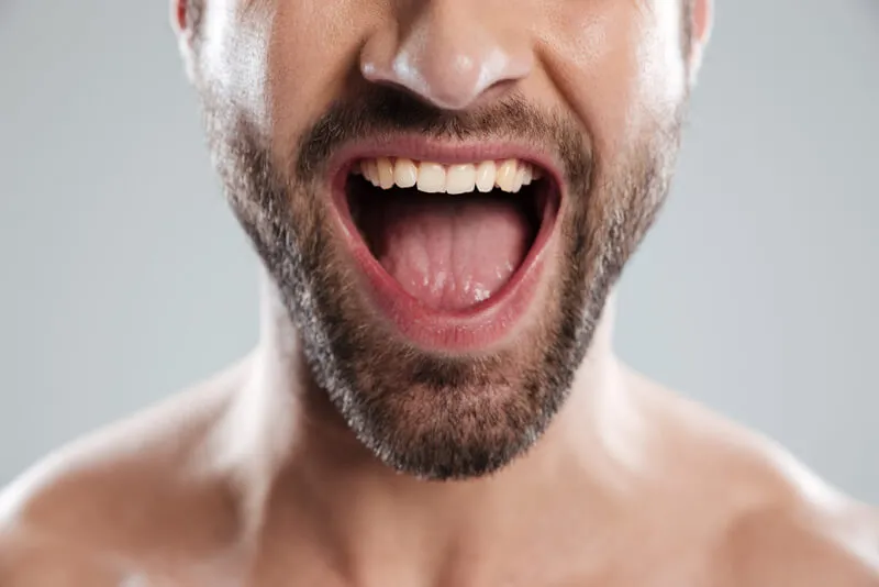 Imagem parcial de um rosto de um homem com a boca aberta sorrindo